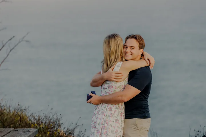 Kayley and Jack embracing by the ocean after the proposal
