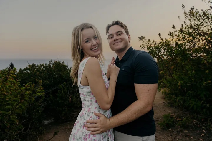 Kayley and Jack smiling together beside the coastal shrubs