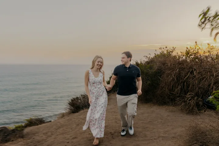 Kayley and Jack walking hand in hand along the ocean bluff