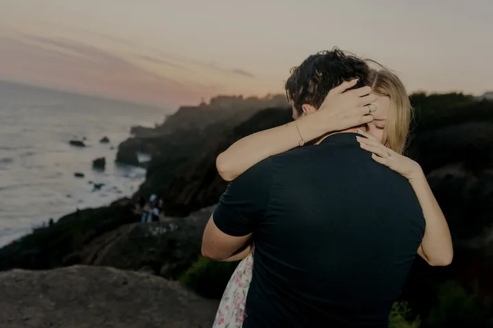 Kayley and Jack embracing with the sunset coastline behind them