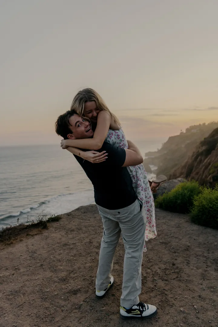 Jack lifting Kayley into an embrace above the coastline