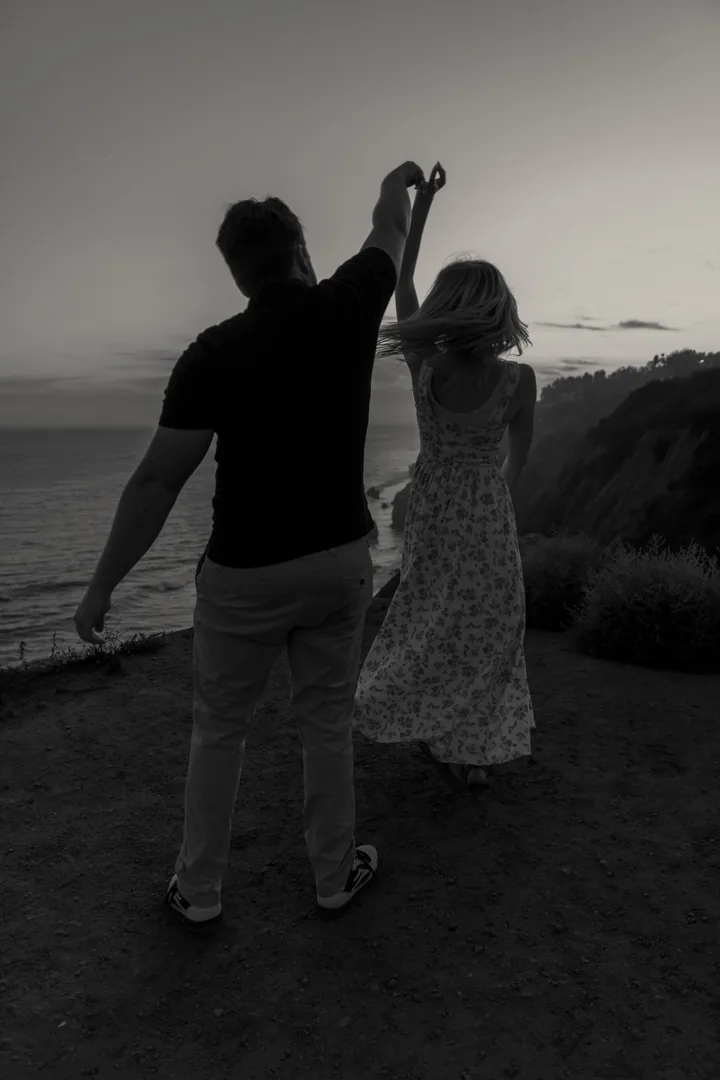 Black-and-white photograph of Kayley twirling beneath their raised hands