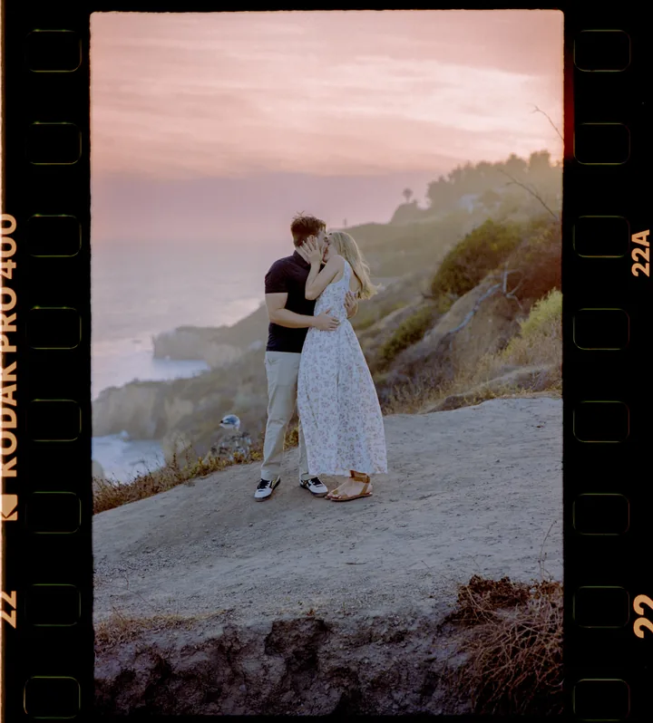 Film-framed portrait of Kayley and Jack embracing above the sunset coastline