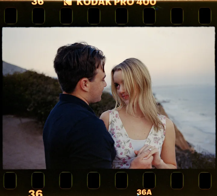 Film-framed portrait of Kayley and Jack facing one another by the ocean